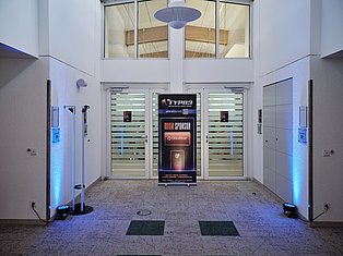 Modern building lobby with glass doors, blue accent lighting, and TYPO3 room sponsor banner