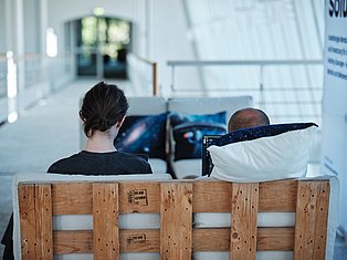 Two people sitting on wooden crate furniture in modern white interior space with blue cushions