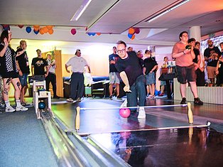 Group of people bowling at an indoor party with colorful balloons and neon lighting