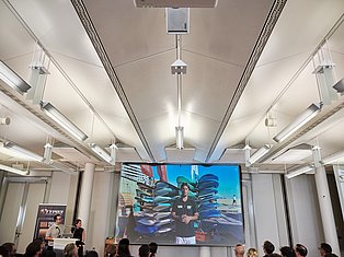 Modern conference room with fluorescent ceiling lights, linear tracks, and large display screen showing water sports presentation