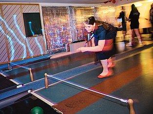 Woman playing mini golf indoors with neon lighting and colorful course obstacles