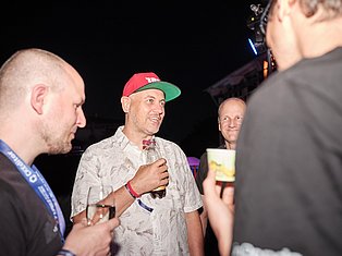 Man in red and green cap talking with people at night event, holding drink