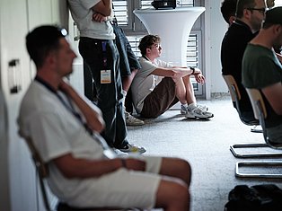 Young man sitting on floor surrounded by people in modern indoor space during group gathering or event