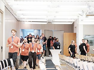 Team members in orange shirts leading a group through a modern conference room with rows of chairs