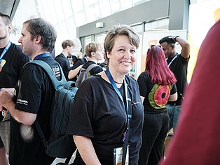 Smiling woman with ID badge at tech conference surrounded by colleagues in black shirts