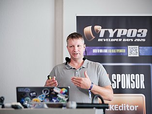 Speaker presenting at TYPO3 Developer Days 2026 conference with microphone and banner backdrop