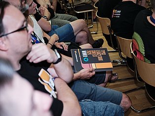 Group of people sitting in chairs at an event, one person holding a branded booklet or program