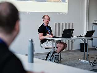 Man presenting at table with laptops during tech conference or workshop in modern office space