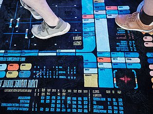 Two people wearing sneakers standing on a digital floor display with colorful data visualization and code