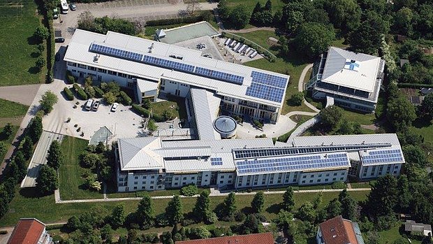 Aerial view of the Geno Hotel in Karlsruhe, showing multiple connected buildings with green courtyards and solar panels on the roofs.
