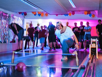Group of people bowling in a neon-lit venue with colorful balloons and vibrant pink and blue lighting