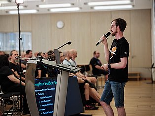 Man speaking at podium with microphone during presentation to seated audience in conference room