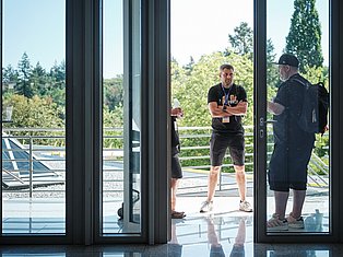 Two men conversing on a modern building terrace with forest views and large glass doors