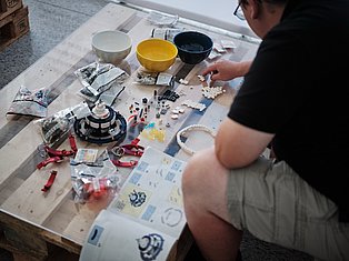 Person assembling craft kit with colorful bowls, beads, and components on wooden table