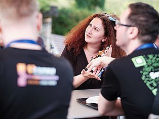 Woman with red curly hair speaking to team members outdoors at an event