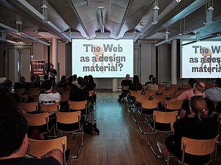 Conference presentation on 'The Web as a design material?' with audience seated in modern auditorium