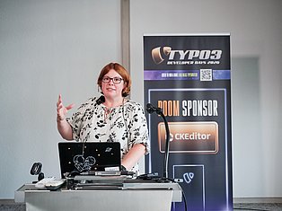 Woman speaking at TYPO3 Developer Days 2020 conference with laptop and microphone at podium