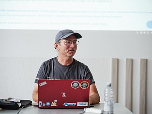 Man wearing glasses and cap working on red laptop with stickers at desk