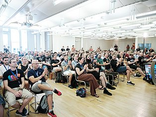 Large audience seated in a bright conference hall watching a presentation or talk