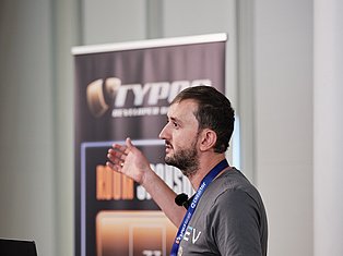 Man with conference badge presenting at podium with branded banner in background