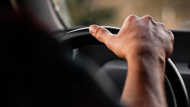 Close-up of a hand gripping a steering wheel while driving.