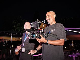 Two men at night event, one holding professional cinema camera with mounted equipment, both smiling