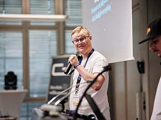 Man with glasses speaking into microphone at conference presentation with projection screen