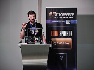 Developer presenting at TYPO3 Developer Days 2026 conference with laptop and headset at podium