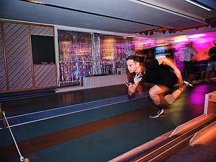 Man exercising in a vibrant nightclub with neon pink and orange lighting, colorful decorations, and other people dancing in the background.