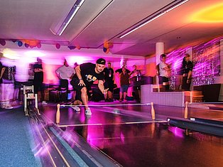 Man playing ping pong in a vibrant neon-lit indoor venue with colorful purple and orange lighting and spectators watching.