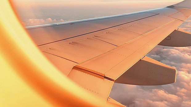 View from an airplane window of the wing above the clouds in warm evening light.