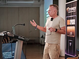 Man speaking at conference with microphone, gesturing expressively near podium with tech branding