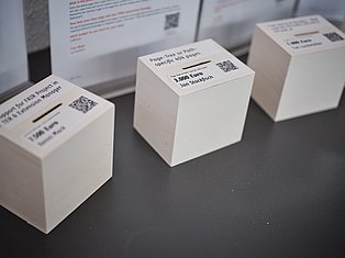 White donation boxes with labels and QR codes displayed on dark surface