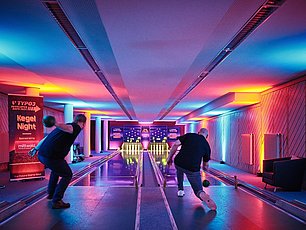 Two people bowling in a neon-lit venue with vibrant pink, blue, and yellow lighting at TYPO3 Developer Days 2025 Kegel Night event.