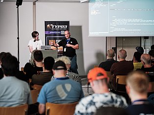 Two speakers present at TYPO3 Developer Days 2020 conference with code displayed on screen behind them
