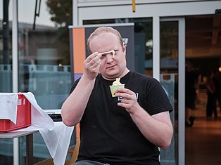 Man in black shirt eating ice cream outdoors in front of modern building