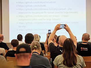 Audience members in lecture hall recording presentation on smartphones and mobile devices