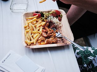 Person eating grilled meat with fries, fresh vegetables and rice from a wooden plate