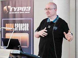 Man speaking at TYPO3 Developer Days 2020 conference with microphone and sponsor banner
