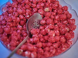Fresh red raspberries in a colander with a slotted spoon on a blue surface