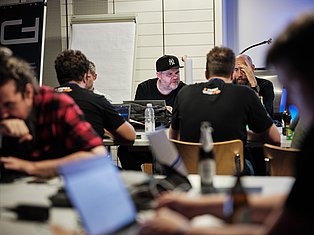 Group of people in a meeting room discussing around a table with laptops and water bottles