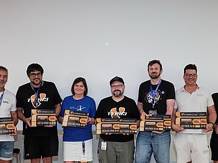 Seven people standing in a line holding award boxes and wearing lanyards against a white wall