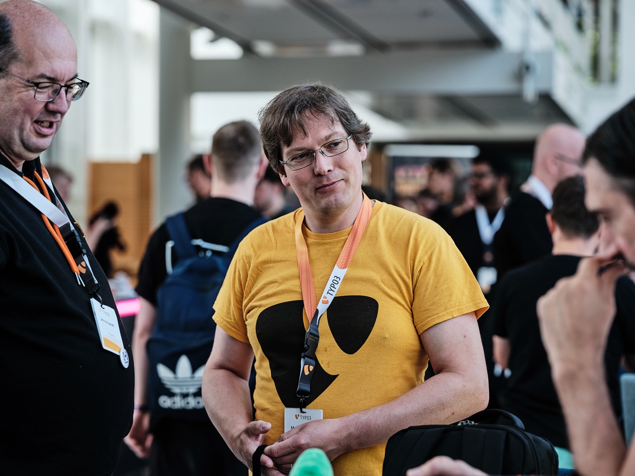 Person wearing a yellow TYPO3 T-shirt and name badge talking with other attendees at TYPO3 Developer Days.
